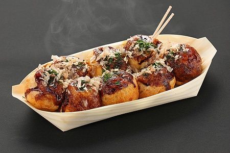 Takoyaki giapponesi in barchetta di legno su sfondo nero.