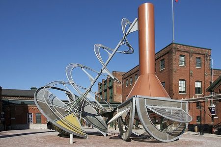 Scultura moderna nel Distillery District di Toronto con edifici storici sullo sfondo.