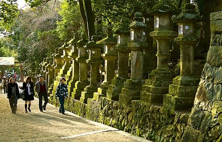 Turisti camminano accanto a lanterne di pietra con muschio al santuario Kasuga Taisha, Nara.