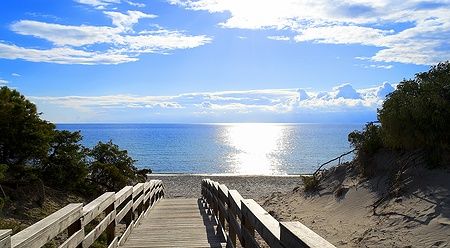La Spiaggia di Maria Pia ad Alghero con passerella e sole riflesso sul mare.
