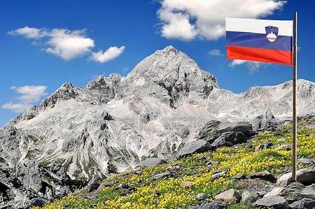 Monte Triglav con bandiera slovena e fiori gialli in primo piano.