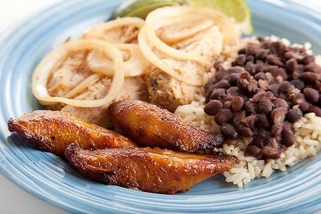 Piatto cubano con platani fritti, maiale, fagioli neri e riso su piatto azzurro.