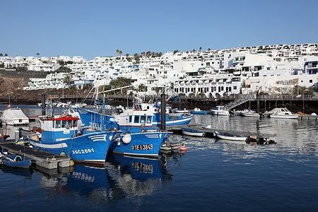 Barche da pesca nel porto di Puerto del Carmen, Lanzarote, con case bianche sullo sfondo.