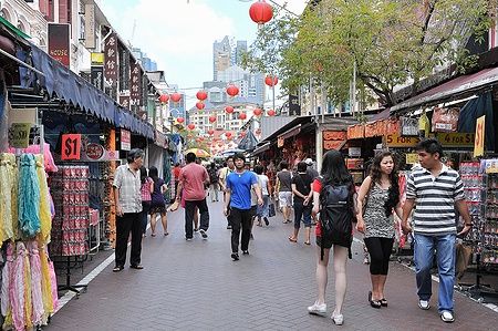 Persone camminano tra le bancarelle a Chinatown, Singapore, con lanterne rosse appese.