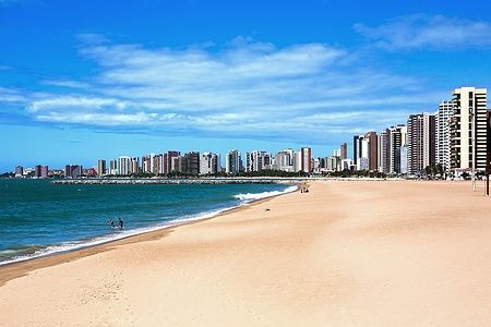 Spiaggia di Fortaleza con grattacieli sullo sfondo e persone in acqua.