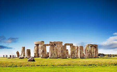 Stonehenge sotto un cielo blu, con persone intorno.