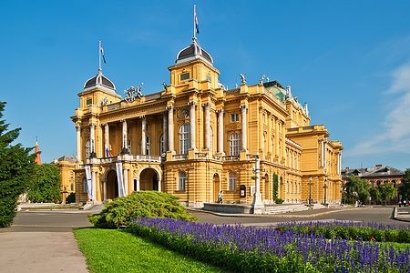 Il Teatro Nazionale Croato a Zagabria sotto un cielo blu, circondato da fiori.