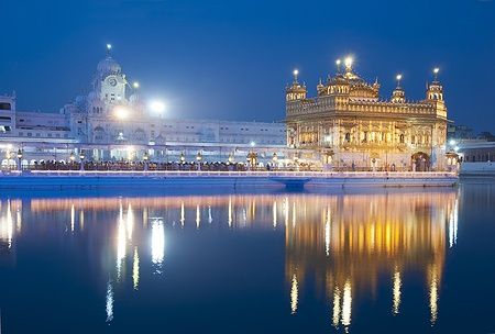 Il tempio d'oro di Amritsar illuminato di notte con riflessi sull'acqua.