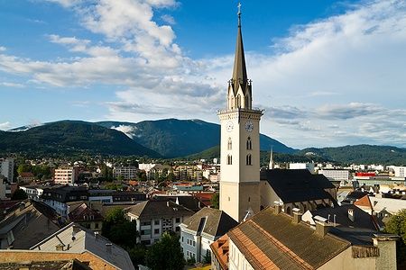 Vista aerea di Villach con chiesa e montagne sullo sfondo.