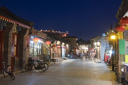 Strada di un hutong a Pechino di notte con negozi illuminati.