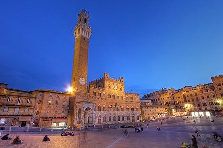 Palazzo Pubblico e Torre del Mangia a Siena al tramonto con persone in Piazza del Campo.