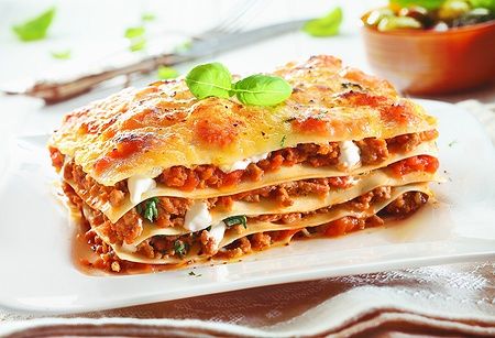 Lasagna tradizionale bolognese con carne macinata e basilico su piatto bianco.