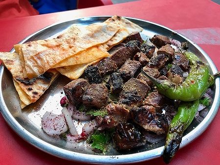 Fegato albanese con cipolle e shawarma su un vassoio con peperoncini e pane piatto.