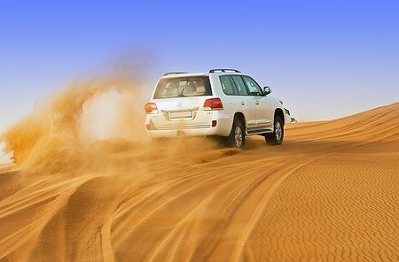 Jeep bianco attraversa le dune del deserto di Dubai, sollevando sabbia.