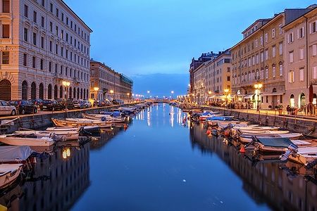Vista notturna del Canal Grande a Trieste con barche e luci cittadine.