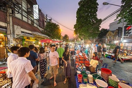 Mercato serale a Chiang Mai con bancarelle e persone sotto un cielo al tramonto.