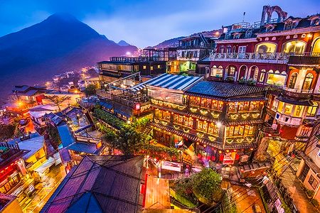 Case da tè di Jiufen illuminate di notte con un paesaggio collinare sullo sfondo.