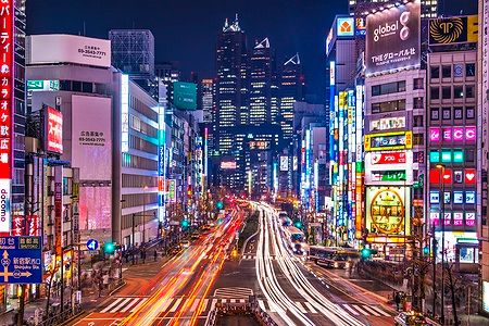 Strada trafficata a Shinjuku, Tokyo, di notte con insegne luminose.