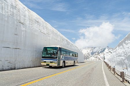 Autobus in movimento lungo un alto muro di neve sulle Alpi giapponesi.