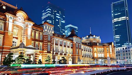 Tokyo Station illuminata di sera con skyline di grattacieli sullo sfondo.
