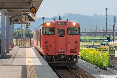 Treno locale alla stazione di Takaoka con montagne innevate sullo sfondo.