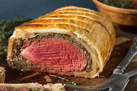 Beef Wellington con crosta dorata su tagliere di legno.