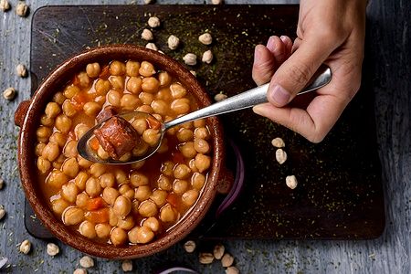 Mano con cucchiaio sopra cocido madrileno, stufato tipico di Madrid.
