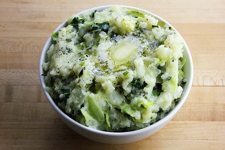 Colcannon fatto in casa con burro fuso su un tavolo di legno chiaro.