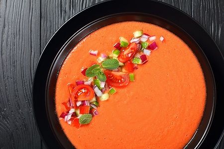 Gazpacho spagnolo con pomodori, cetrioli e cipolla rossa su piatto nero.