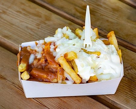 Porzione di patatine fritte belghe con cipolla, ketchup e salsa satay su tavolo di legno.