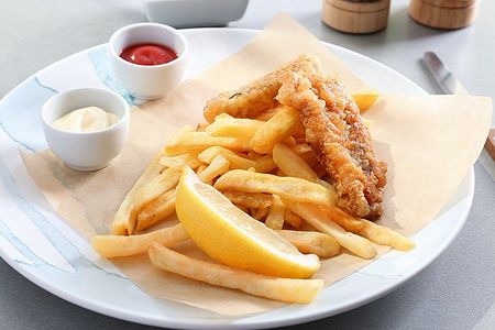 Piatto con pesce fritto, patatine e salse su tavolo.