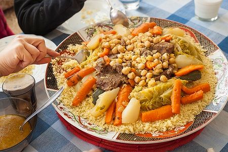 Piatto di couscous marocchino con verdure e carne su tavola imbandita.