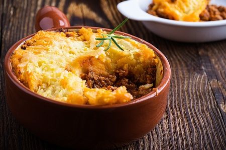 Shepherd's pie tradizionale britannico con carne macinata e purè di patate su tavolo rustico.