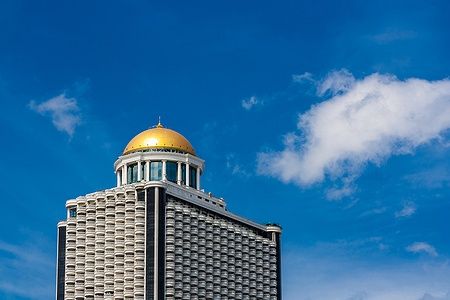 La cupola dorata della State Tower a Bangkok contro un cielo azzurro.