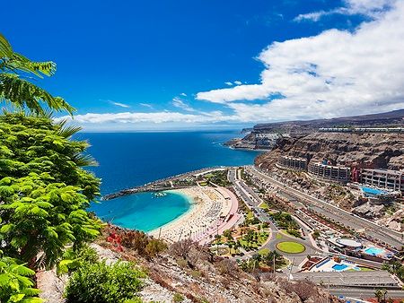 Spiaggia di Amadores vista dall'alto, con mare azzurro e strutture turistiche.