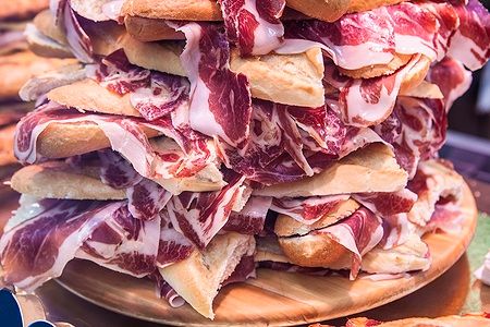 Pila di bocadillos spagnoli con prosciutto serrano su un piatto di legno.