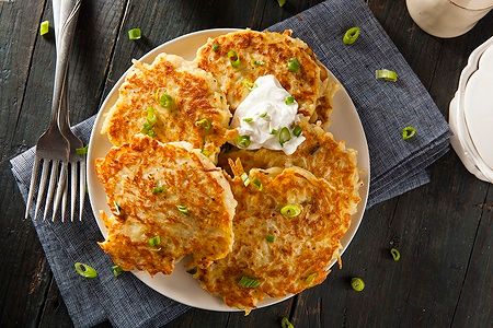 Frittelle di patate Boxty dorate con cipollotto e panna acida su piatto bianco.
