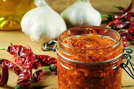 Barattolo di harissa con peperoncini e aglio su tavolo di legno.