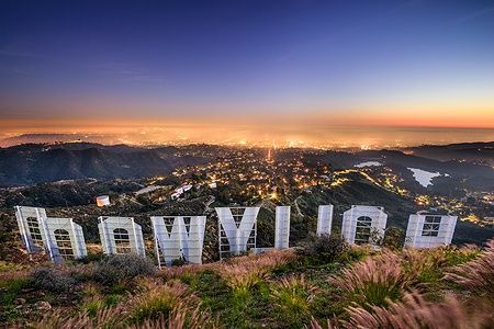 Vista del segno di Hollywood al tramonto con Los Angeles illuminata sullo sfondo.