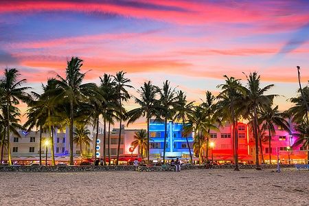 Ocean Drive a Miami Beach con edifici illuminati e palme al tramonto.