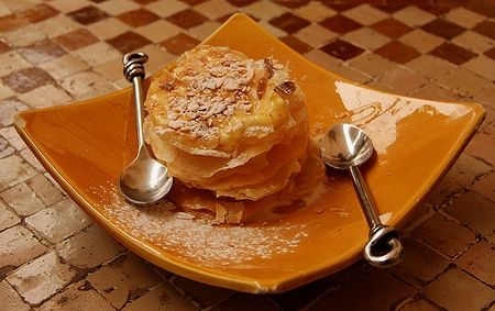 Dessert di pastilla tradizionale con mandorle e zucchero a velo su piatto giallo.