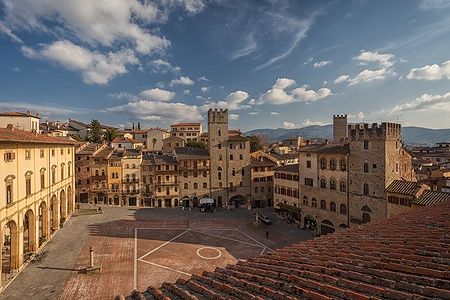 Piazza Grande ad Arezzo con edifici medievali e cielo parzialmente nuvoloso.