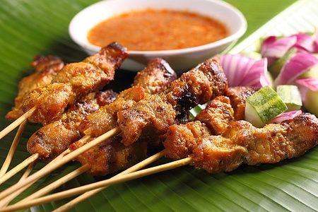Spiedini di pollo satay malese con salsa di arachidi su foglie di banana.