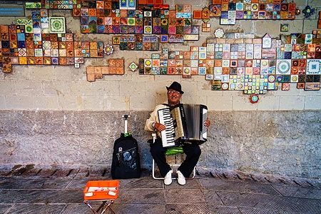 Musicista di strada suona la fisarmonica davanti a un mosaico colorato alle Cinque Terre.
