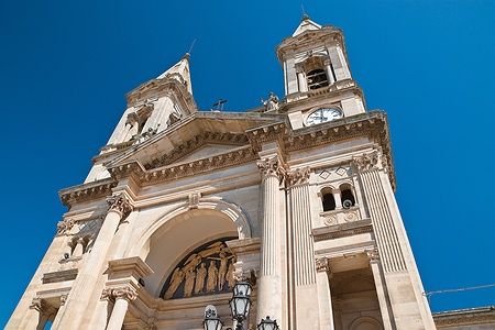 Facciata della Basilica dei Santi Cosma e Damiano ad Alberobello sotto un cielo azzurro.
