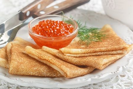Blini russi tradizionali con caviale di salmone su un piatto bianco.