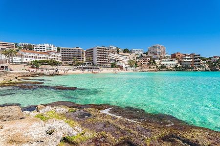 Spiaggia di Cala Major a Maiorca con mare turchese e edifici sullo sfondo.