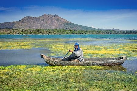 Uomo in canoa su lago Batur, Bali, con sfondo montuoso.