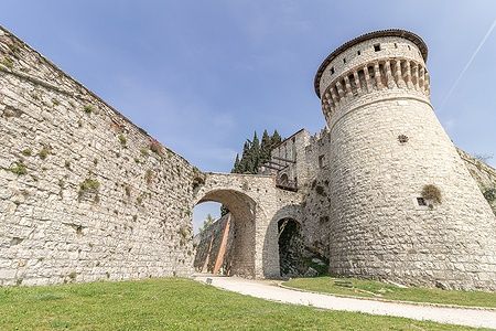 Castello di Brescia con torri e mura medievali sotto il cielo azzurro.