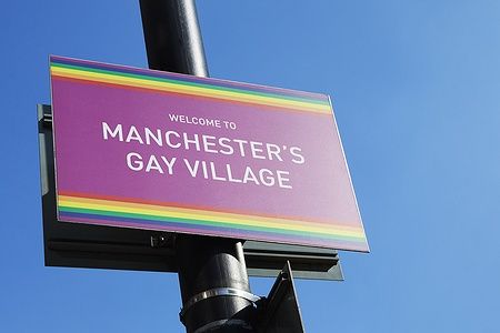 Cartello "Welcome to Manchester's Gay Village" contro un cielo blu.